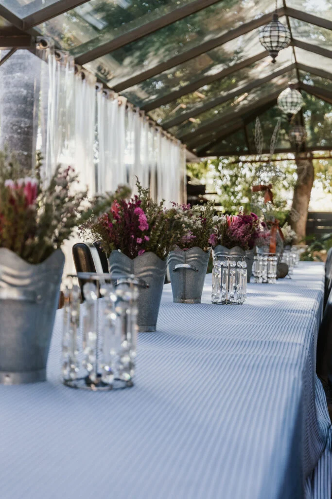 Dining table with flower arrangements beneath the glass-roofed conservatory.