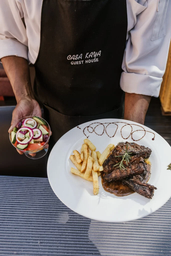 Casa Kaya staff member serving a plated meal with salad and chips.